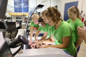 Girls place wood in a laser cutter at the Discovery Center Fab Lab on campus.