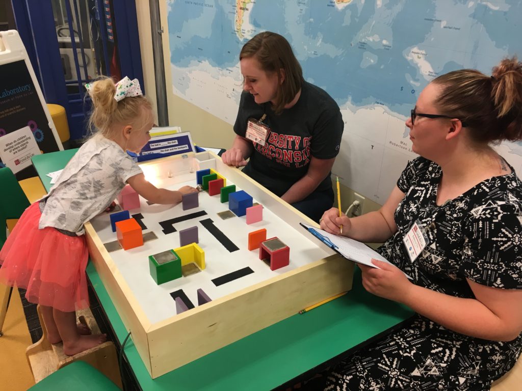 Photo of Clara Wojkiewicz (left) participating in an activity at the Children's Museum of Fond du Lac while UW-Fond du Lac students Grace Hudson (center) and Becky Vis (right) monitor her progress.