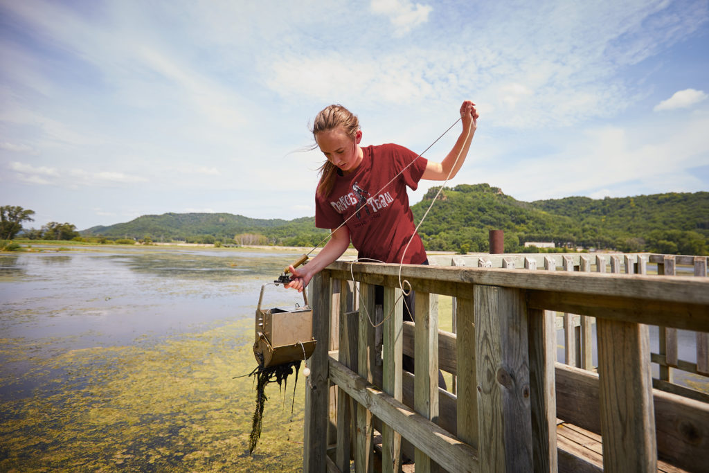 Photo of UWL graduate student Anna Hilger pulling up marsh water and sediment from La Crosse’s Myrick Marsh. The water will be mixed with crude oil for testing.