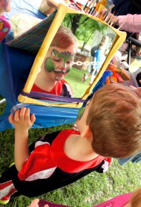 child with face paint looks into a mirror and smiles