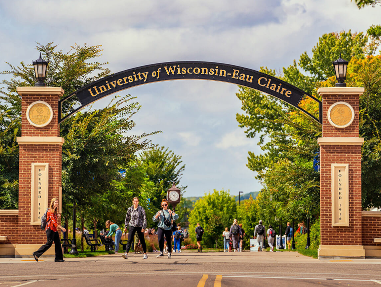 College students walk beneath an outdoor brick and metal arch that reads University of Wisconsin-Eau Claire.