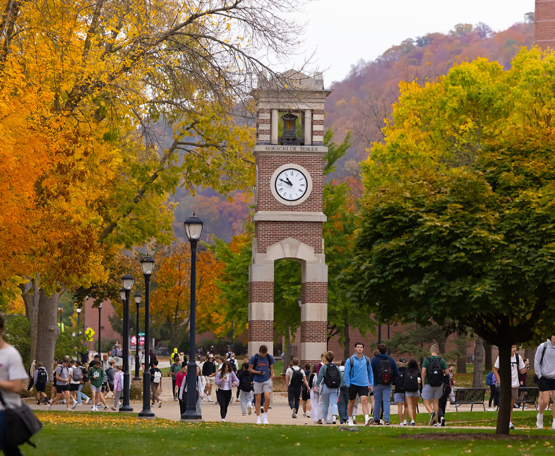 Outdoor view of the UW-La Crosse brick clock tower on a sunny fall day while students walk on the sidewalk below.