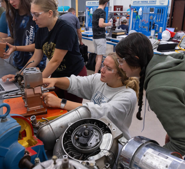 Two female students perform mechanical equipment checks at a table.
