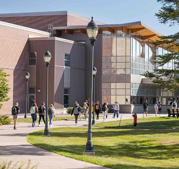 Outdoor view of an academic building with students walking on the sidewalk out front.