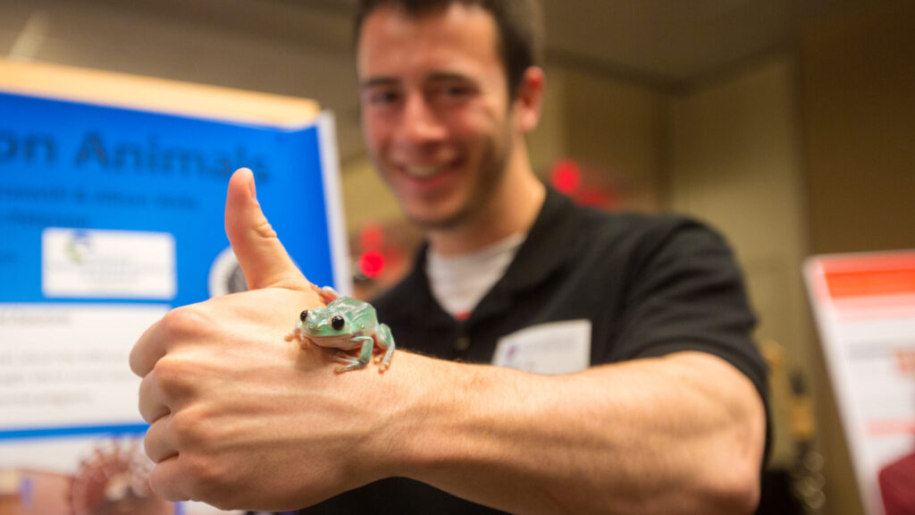 Student presenting poster with a frog on hand.