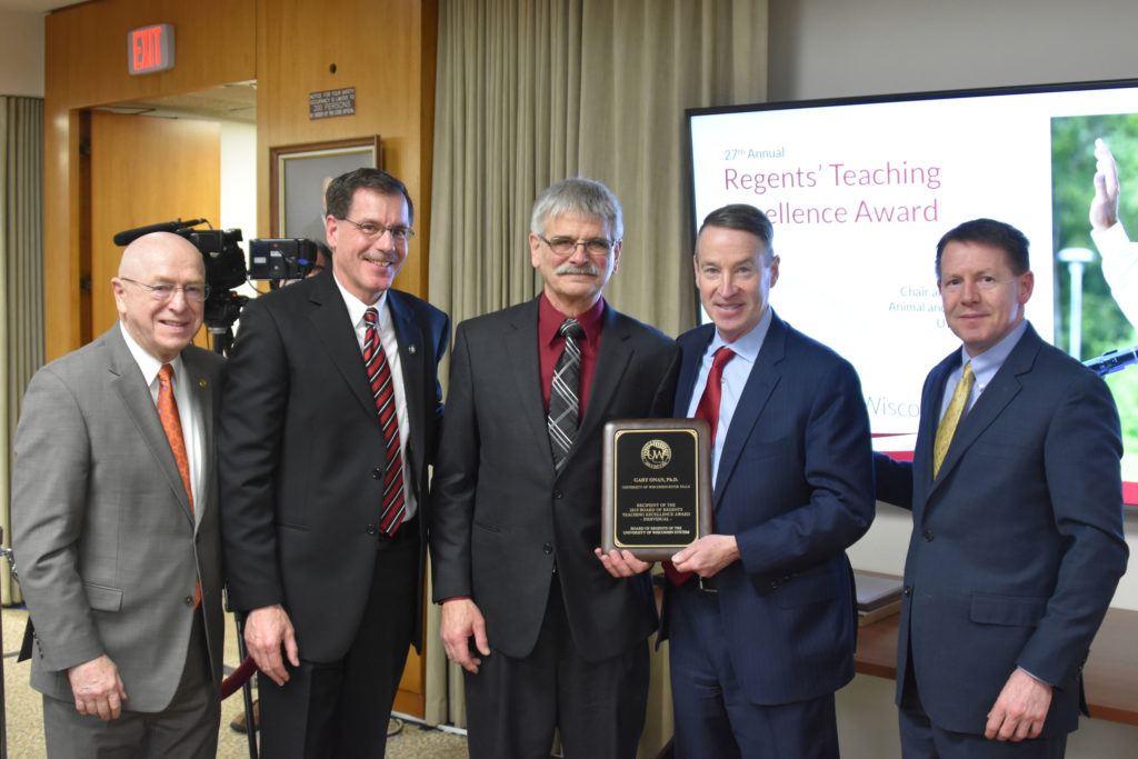 Photo of Gary Onan, Chair and Professor of Animal and Food Science at UW-River Falls (center), receiving a UW System Board of Regents 2019 Teaching Excellence Award at the Board of Regents meeting held in Madison on April 5, 2019. Also pictured (from left): UW System President Ray Cross, UW-River Falls Chancellor Dean Van Galen, Regent Mike Jones, and Regent President John Robert Behling.