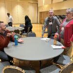 Colleagues sitting or standing at round tables chatting at UW System Navigate and Advising Workshop March 2023 at UW-Stevens Point