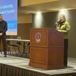 Sue Buth of UW System at podium introducing Matt Petersen of Northeast Wisconsin Technical College (standing in front of his projected powerpoint slide) at the March 2023 workshop at UW-Stevens Point