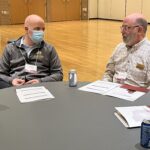 2 colleagues seated at a table talking to each other at the UW System Navigate and Advising Workshop March 9, 2023, at UW-Stevens Point