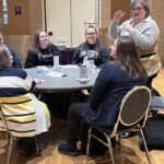 Amy McGovern of UW-Stout standing and gesturing to 5 UW-Stout colleagues seated at a table at the UW System Navigate and Advising Workshop March 9, 2023, at UW-Stevens Point