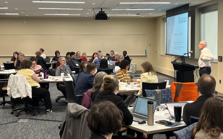 Universities of Wisconsin Senior Vice President Johannes Britz is standing in front of a Pyle Center meeting room to address campus teams from across the system who are seated at tables. Click on the image and log in with your UW email credentials to access workshop materials.